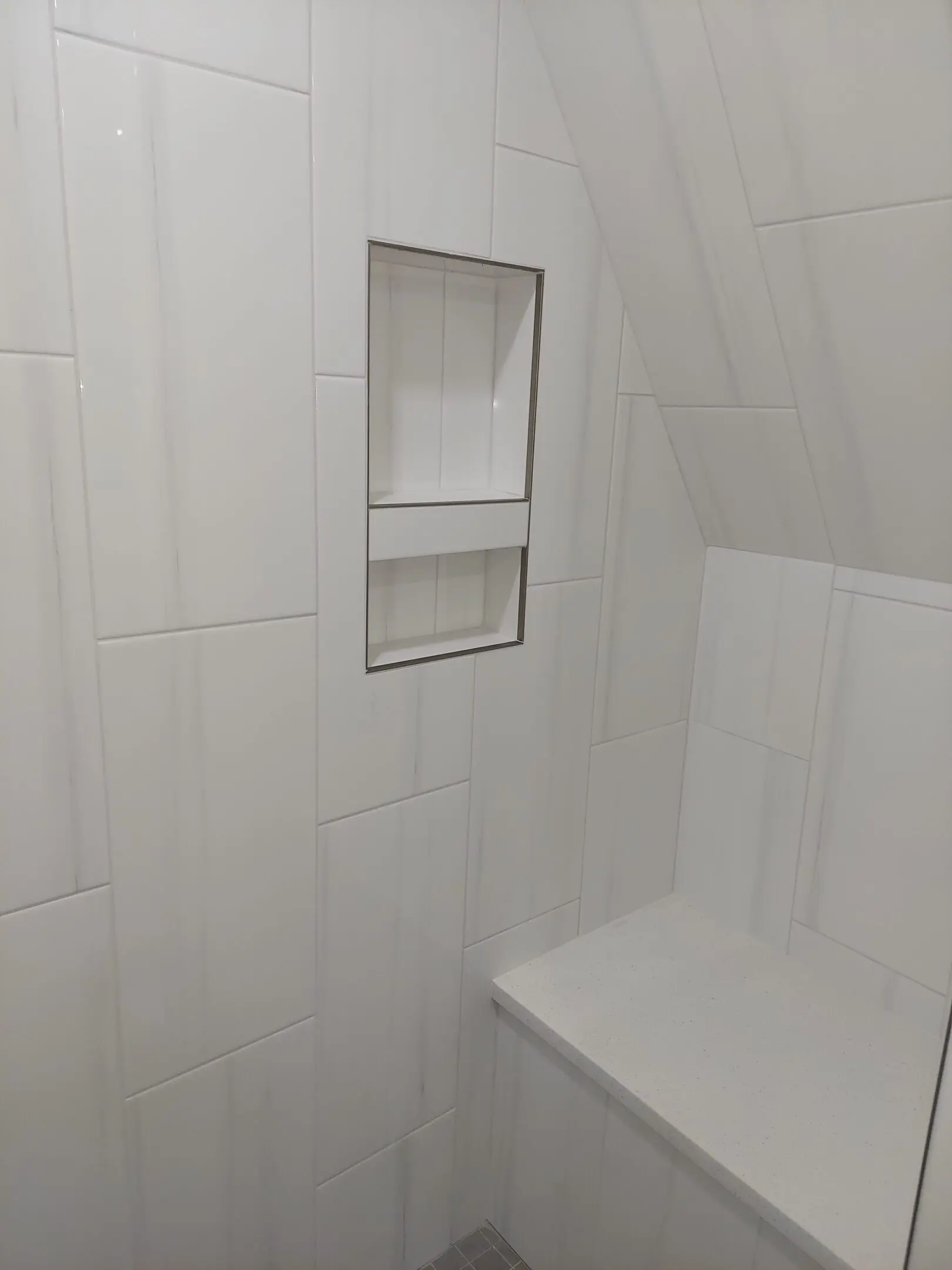 White tiled shower with built-in shelf.
